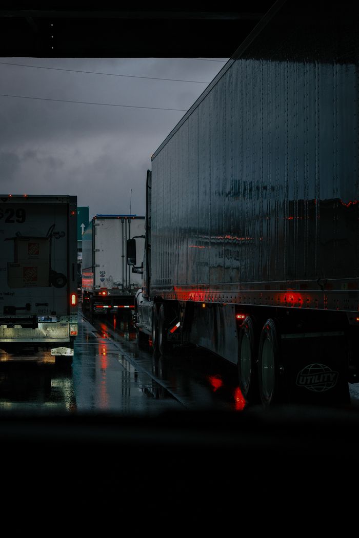 Trucks lined up on a rainy highway with reflections and brake lights under dark clouds.